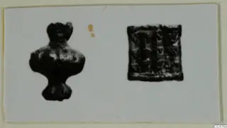 Two small dark objects on a pale card: a figure-like piece on the left and a square piece with a patterned surface on the right.