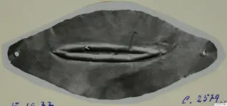 Thin lens-shaped metal ornament with two small holes at its ends, from Enkomi, shown on a mounted card.
