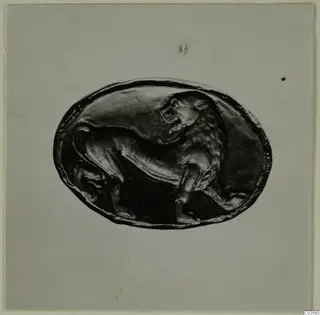 Oval dark bezel with a lion carved in relief, photographed on a pale grey card