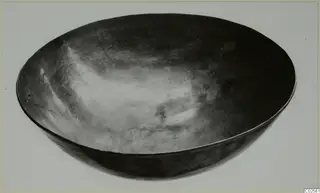 Shallow bowl with a smooth, dark surface and rounded walls, photographed on a pale background