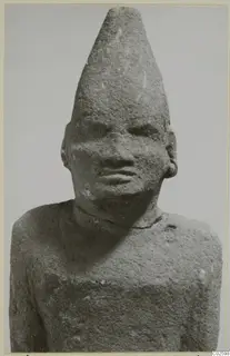 Limestone Cypro-Egyptian sculpture of a head and upper torso with a tall conical cap, seen from the front.