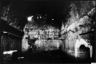 Interior of a built tomb chamber with a stone bench on the left and an arched niche in the right wall