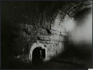 Interior of a built tomb with a stone vault and a low arched doorway in the wall