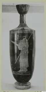 Tall dark vessel with a cup-shaped mouth and a light-toned standing figure holding a spear, on a small base
