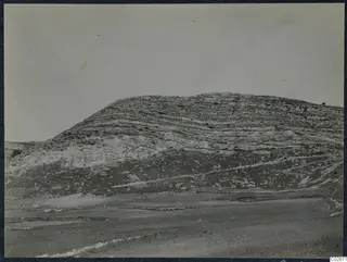 Layered limestone hill rising above open ground, with a faint track running across its slope.