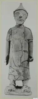 Terracotta standing figure in a pointed cap and short-sleeved robe, seen from the front, with cracks and visible joins.