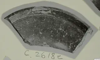 Curved pottery sherd with a dark surface and pale flaked patches, photographed on a card with a handwritten number label