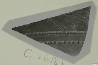 Triangular pottery sherd with horizontal ridged bands and diagonal grooves, shown on a grey card mount