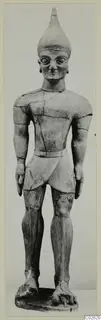 Standing terracotta male figure with a conical headdress, large eyes and a belt, on a rectangular base