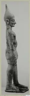 Standing terracotta figure in profile, with a tall conical headdress and arms held close to the body