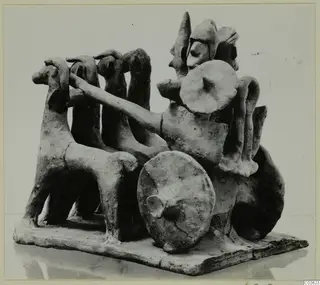 Terracotta model of a chariot drawn by a team of horses, with a standing driver holding the reins, on a flat base.