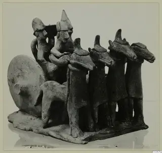 Terracotta group of small figures on a shared base, including a row of four standing figures with animal-like heads and a quadruped.