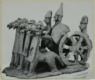 Terracotta model of a chariot drawn by horses, with three figures and a spoked wheel, on a flat base.