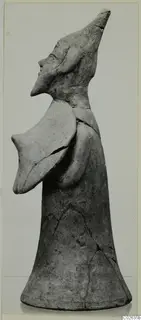 Terracotta figurine in profile, with a tall flaring body, a pointed head with a beaked face, and a flat projection at the shoulder.