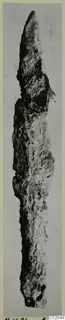 Corroded iron spearhead, a long narrow blade tapering to a point, with two small holes near the lower end.