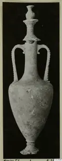 Alabaster vessel with two handles and a tall stacked stopper, photographed against a black background