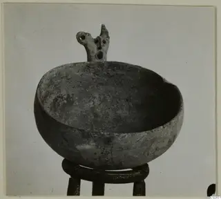 Black Slip Ware bowl with a pierced projection on its rim, shown on a ring-shaped stand