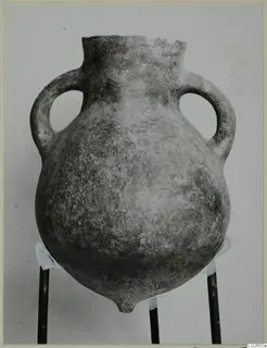 Two-handled pottery vessel with a rounded body and broken rim, photographed upright on a three-legged stand