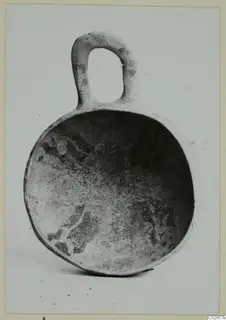 Pottery bowl with a loop handle, interior showing dark painted decoration on a pale surface.