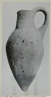 Pottery bottle with a single loop handle and pointed base, photographed against a plain grey background.