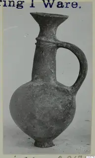 Juglet of Base-Ring Ware with a flaring mouth, strap handle and ring base, photographed on a plain background