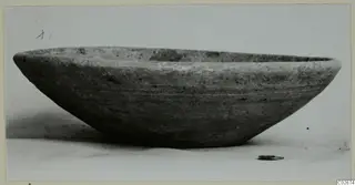 Wheel-made plain bowl with a wide, shallow body, photographed from the side on a pale surface.