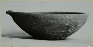 Plain white wheel-made bowl with a small handle projecting from the rim, seen from the side