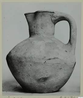 Pottery jug, plain white wheel-made, with one strap handle and a pinched spout, photographed against a plain backdrop