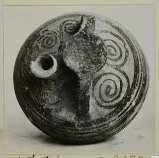 Painted stirrup jar from Ayios Iakovos with a spout and strap handle, decorated with dark spirals and bands.