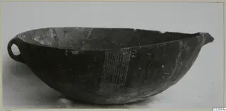 Deep bowl with a small loop handle and pale vertical hatched bands on its dark body, seen in profile
