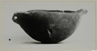 Side view of a dark pottery bowl with a pierced lug at the left and a horizontal handle at the right
