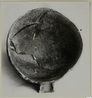 Pottery bowl with a small handle, seen from above, with cracks across its dark surface