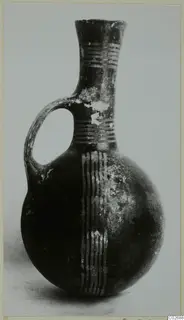 Dark jug with a single loop handle, a flaring neck and pale painted bands on the neck and body.
