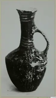 Jug with a single loop handle and banded neck, dark surface with pale patches of wear.