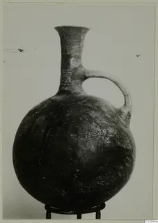 Round-bodied jug with a tall flaring neck and single loop handle, with incised dashes on neck and shoulder, shown on a metal ring stand
