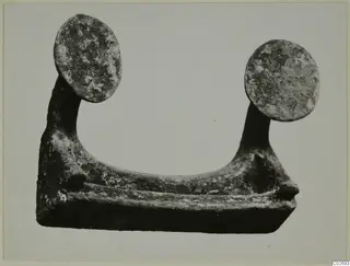 Corroded bronze object with two flat round discs on upright stalks, photographed against a pale background