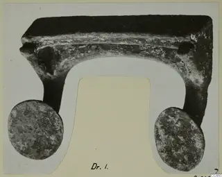 Corroded metal object from Marion with a flat top bar, a curved underside and two round discs at its ends