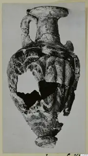 Sand-core glass amphoriskos from Marion Tomb 7, with a ribbed body and a loop handle on one side.