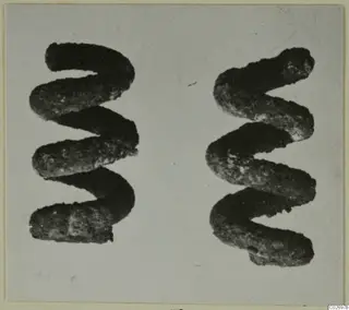 Two bronze spiral objects, each coiled in a zigzag form, photographed side by side on a pale background.