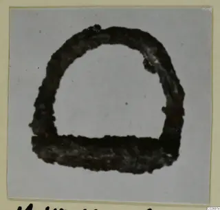 Corroded iron tool, semicircular with a flat base, shown close up on a mounted photograph card.