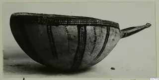 Bowl with a long handle to the right, decorated with dark painted bands and cross-hatching, photographed in side view
