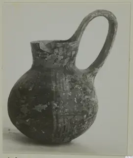 Red-on-Black pottery jug with a tall loop handle, photographed against a plain pale background