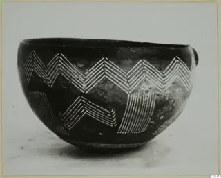 Dark polished bowl with white-painted zigzag and hatched bands, photographed against a pale background.