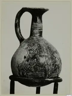Pottery Red Polished II jug with a single loop handle and banded linear decoration, shown on a stand