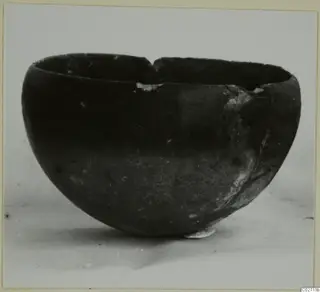 Red Polished II bowl, a dark rounded bowl with a broken rim photographed on a pale surface.