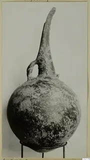 Red Polished II jug with a tall, tapering neck and a loop handle, standing on a wire stand
