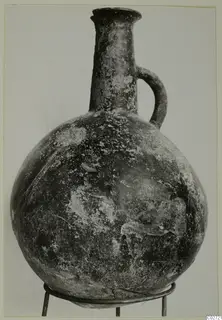 Round-bodied jug with a tall neck and single loop handle, standing on a wire stand against a plain background.