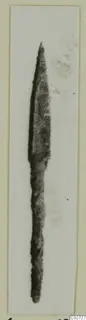 Bronze arrowhead, long and narrow with a pointed tip and slender shank, photographed on a pale card mount