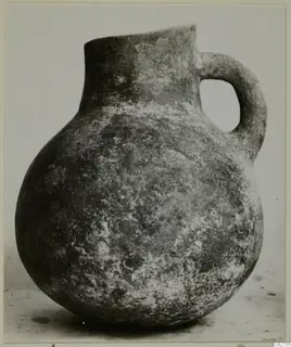 Jug with a rounded body, tall neck and strap handle, photographed against a plain background