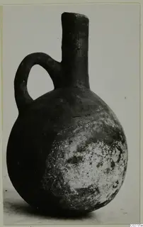 Black-slipped jug with a single loop handle and tall neck, photographed against a plain background.